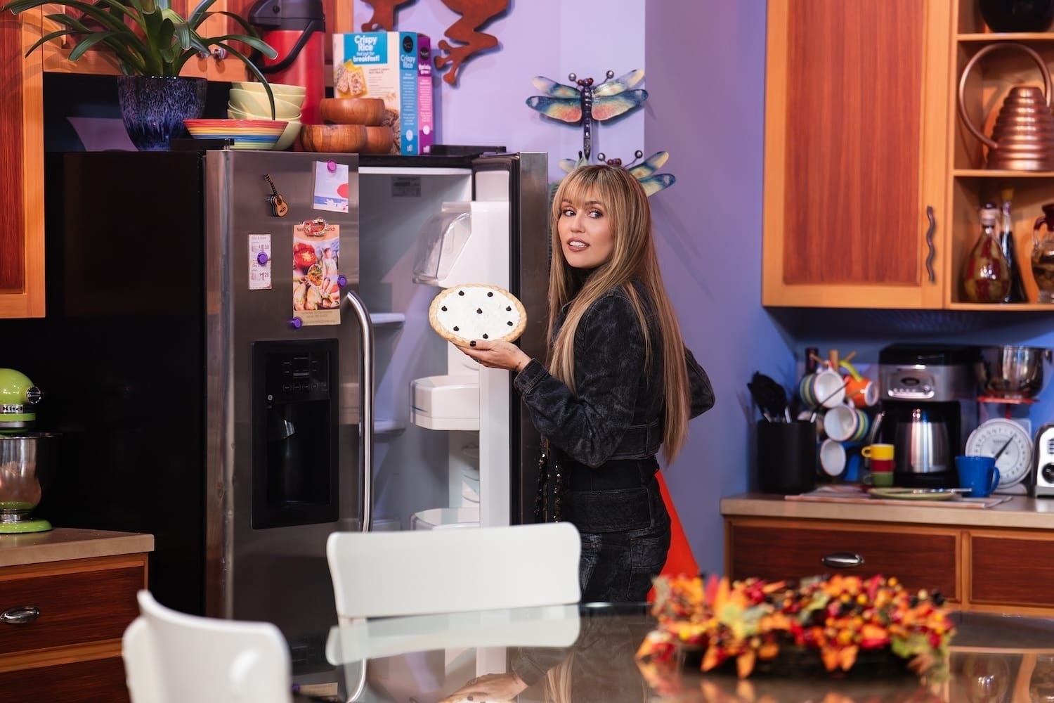 Miley inside the Stewarts' perfectly recreated kitchen. She's standing in front of the fridge, holding the pie from the show's pilot.